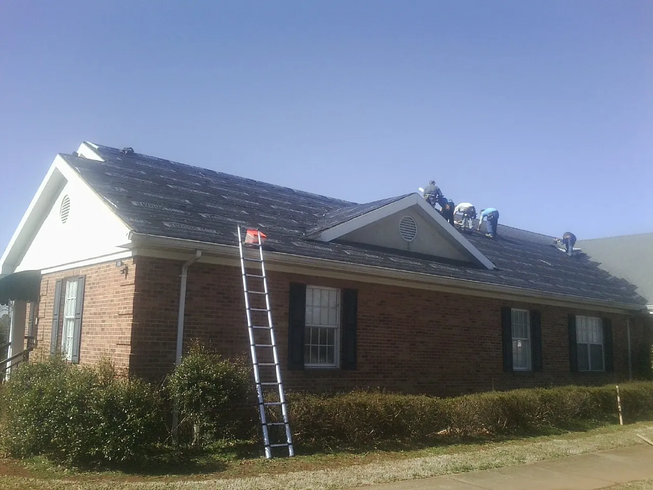 Crew tearing shingles off a brick ranch roof with a ladder set — Metal Roof Repair work by our crew in Rio
