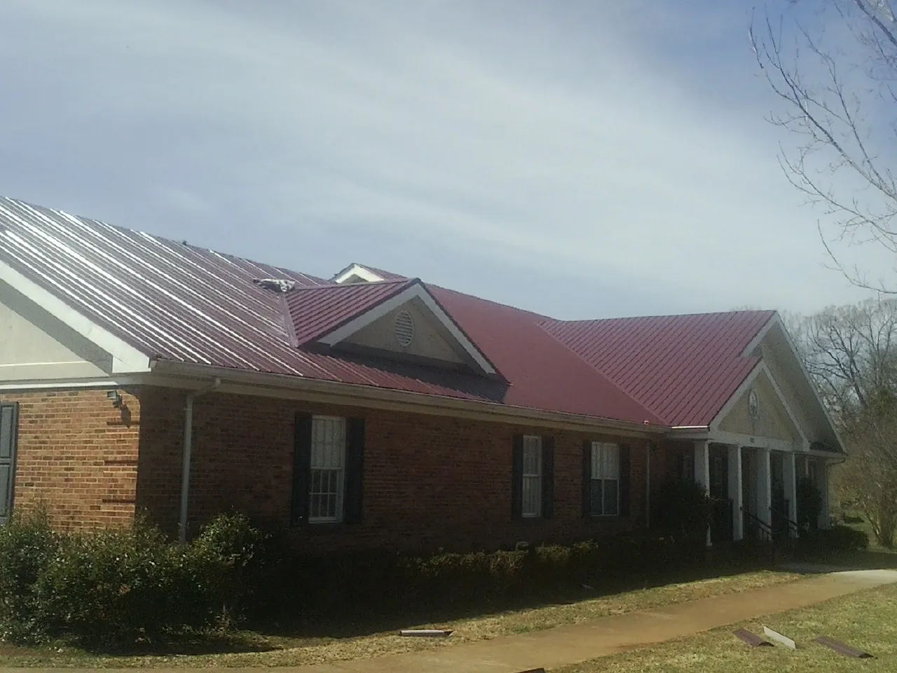 Red metal roof with gabled entries on a long brick building, from a Hail Damage Roof Repair job in Rio