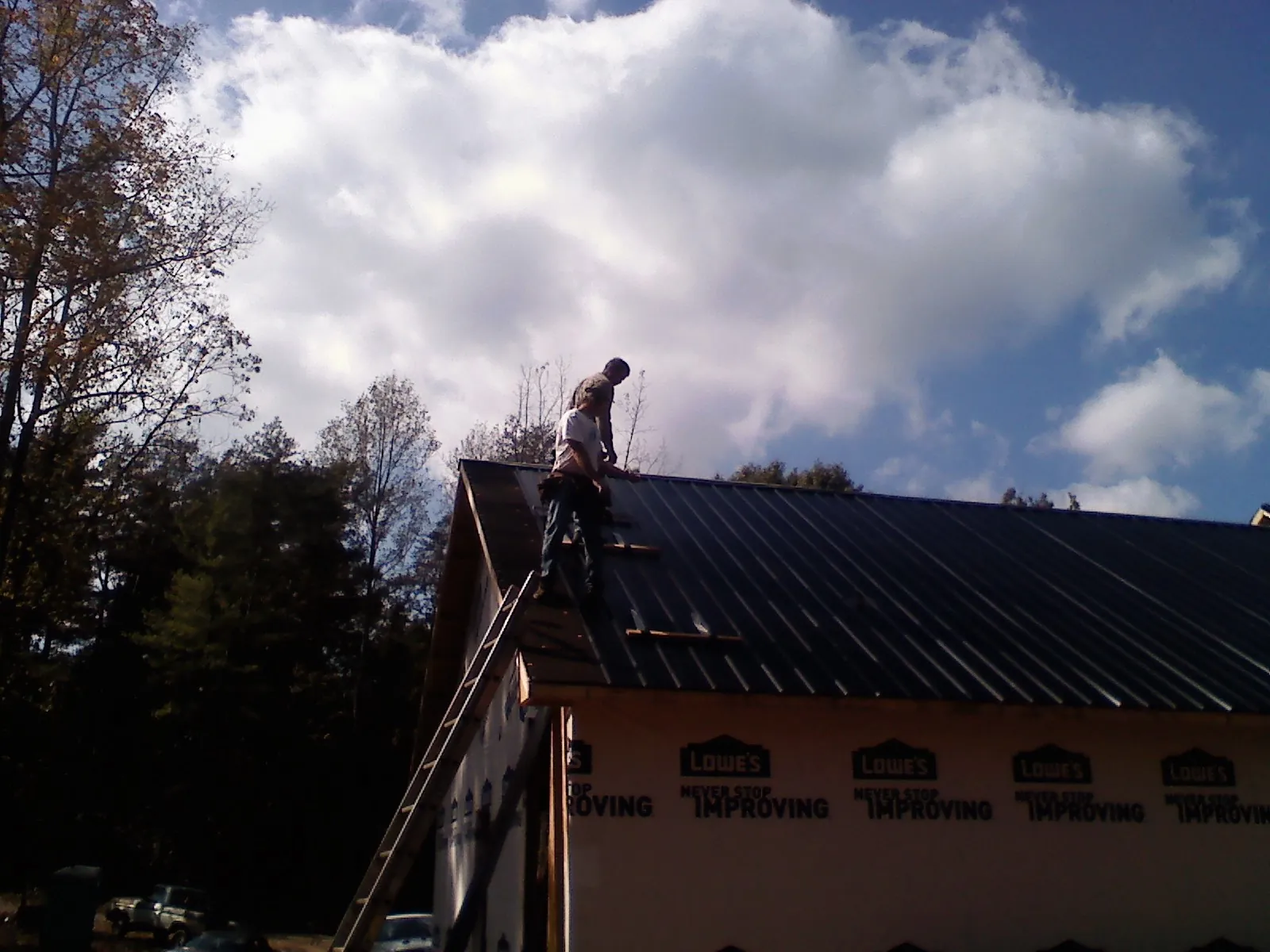 Roofer fastening dark metal panels high against a cloudy sky, from a Roof Inspection job in Rio
